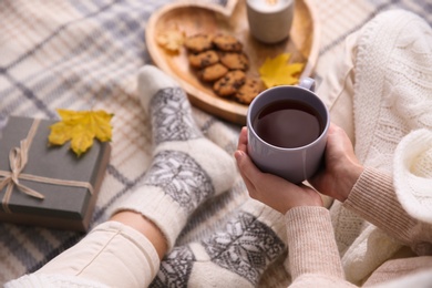 Woman relaxing with cup of hot winter drink on checkered plaid, closeup. Cozy season