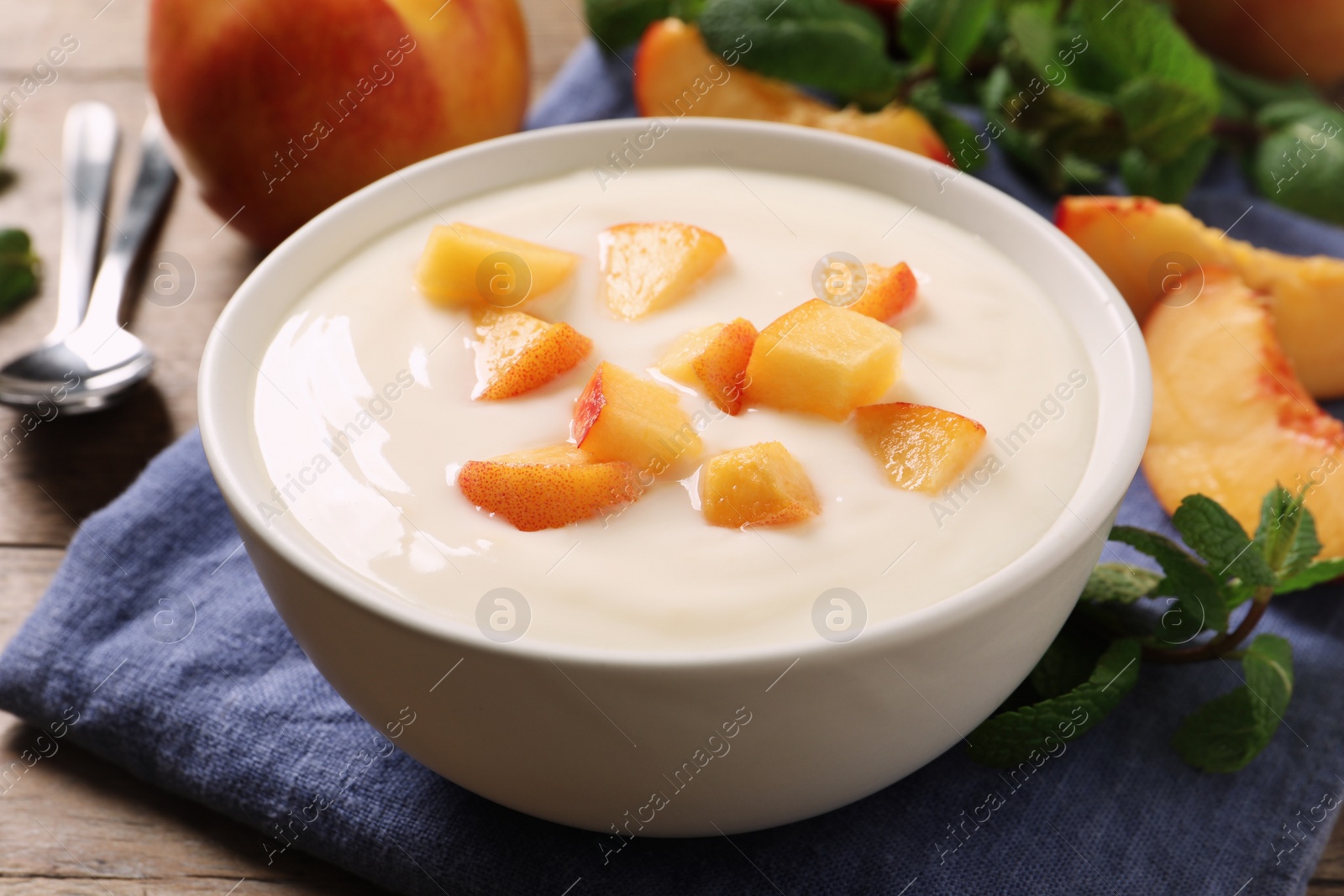 Photo of Delicious yogurt with fresh peach on wooden table, closeup