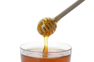 Honey dripping from dipper into jar on white background