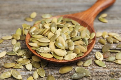 Photo of Spoon with pumpkin seeds on wooden table, closeup