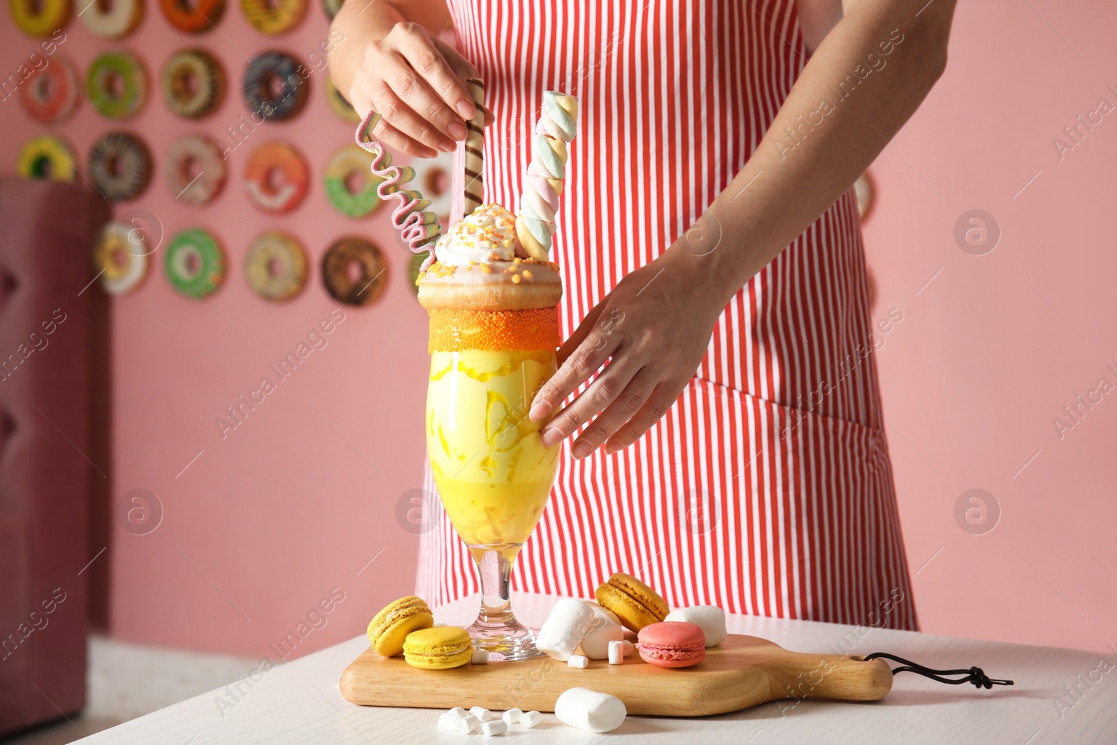 Photo of Woman preparing tasty milk shake with sweets at table indoors