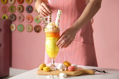 Woman preparing tasty milk shake with sweets at table indoors