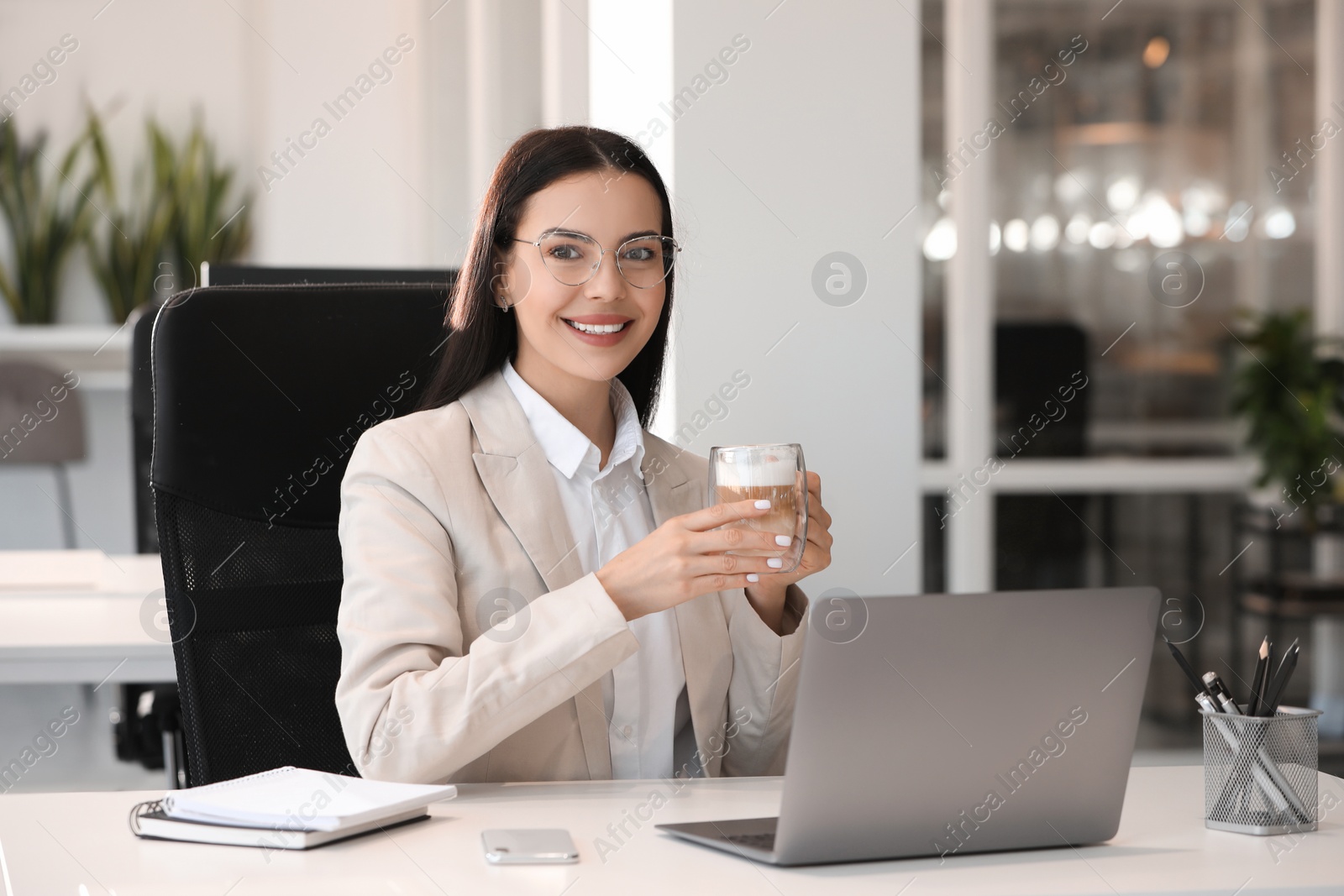 Photo of Happy woman with cup of coffee using modern laptop at white desk in office