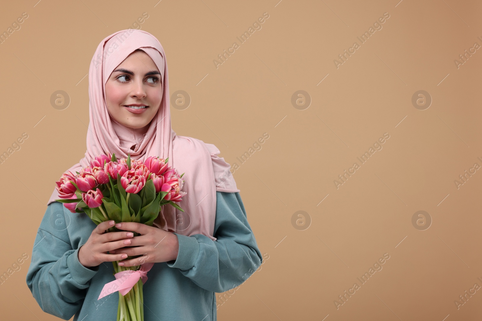 Photo of Happy woman in hijab with beautiful bouquet on beige background. Space for text