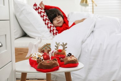 Photo of Cute little boy sleeping in bed at home, focus on slippers with treats. Saint Nicholas day tradition