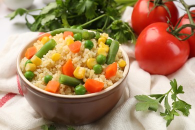 Photo of Delicious bulgur with vegetables in bowl, tomatoes and parsley on table, closeup