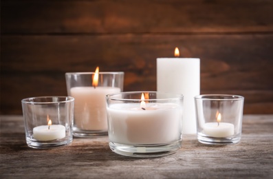 Photo of Burning wax candles in glasses on wooden table