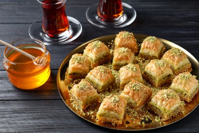 Photo of Delicious fresh baklava with chopped nuts served on black wooden table. Eastern sweets