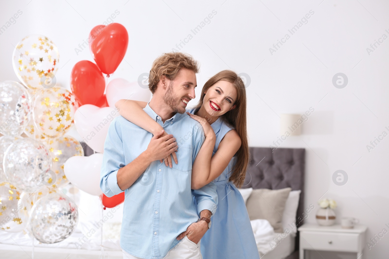 Photo of Young couple with air balloons in bedroom. Celebration of Saint Valentine's Day