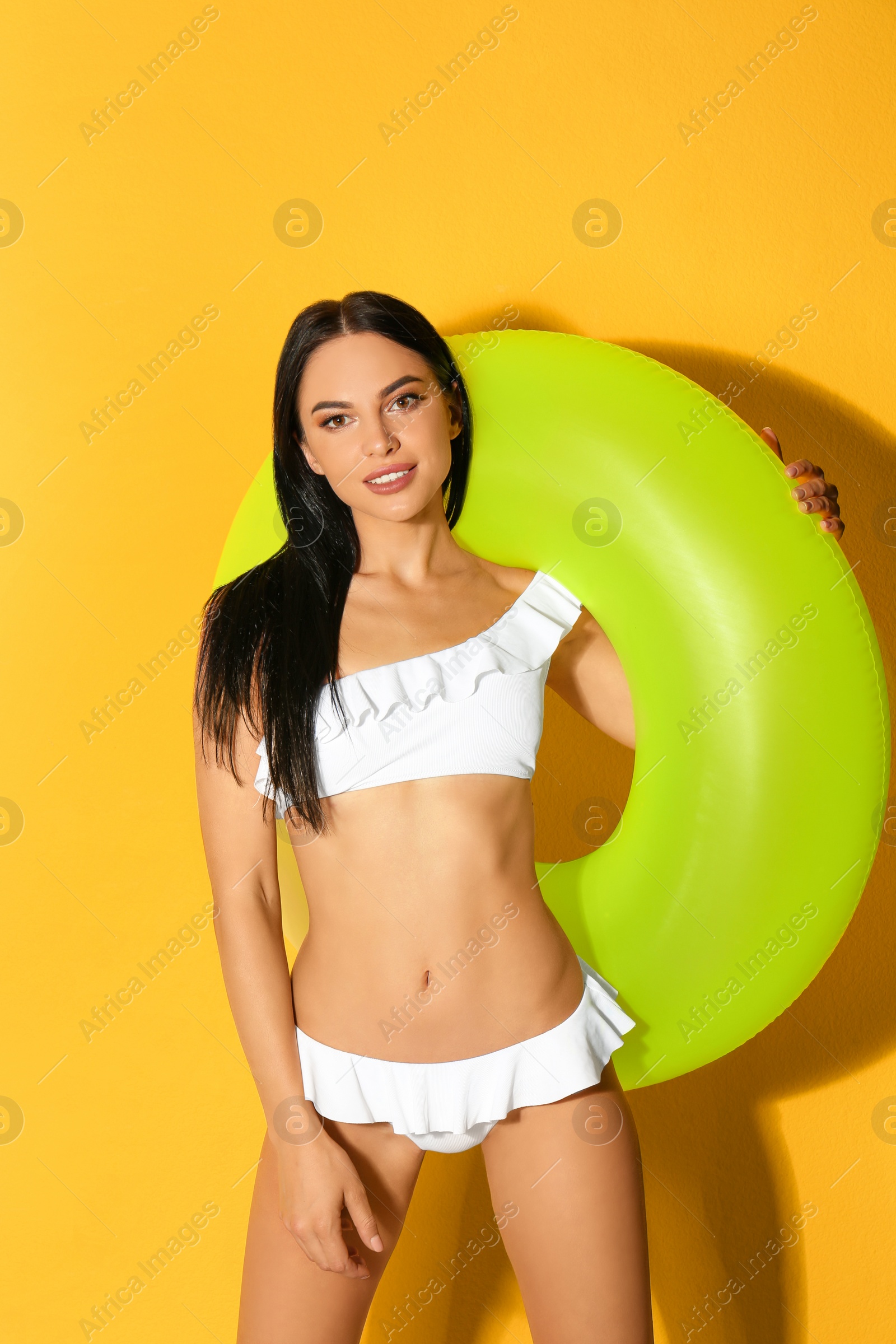 Photo of Beautiful young woman in white bikini with inflatable ring on yellow background