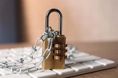 Photo of Cyber security. Keyboard with padlock and chain on wooden table, closeup