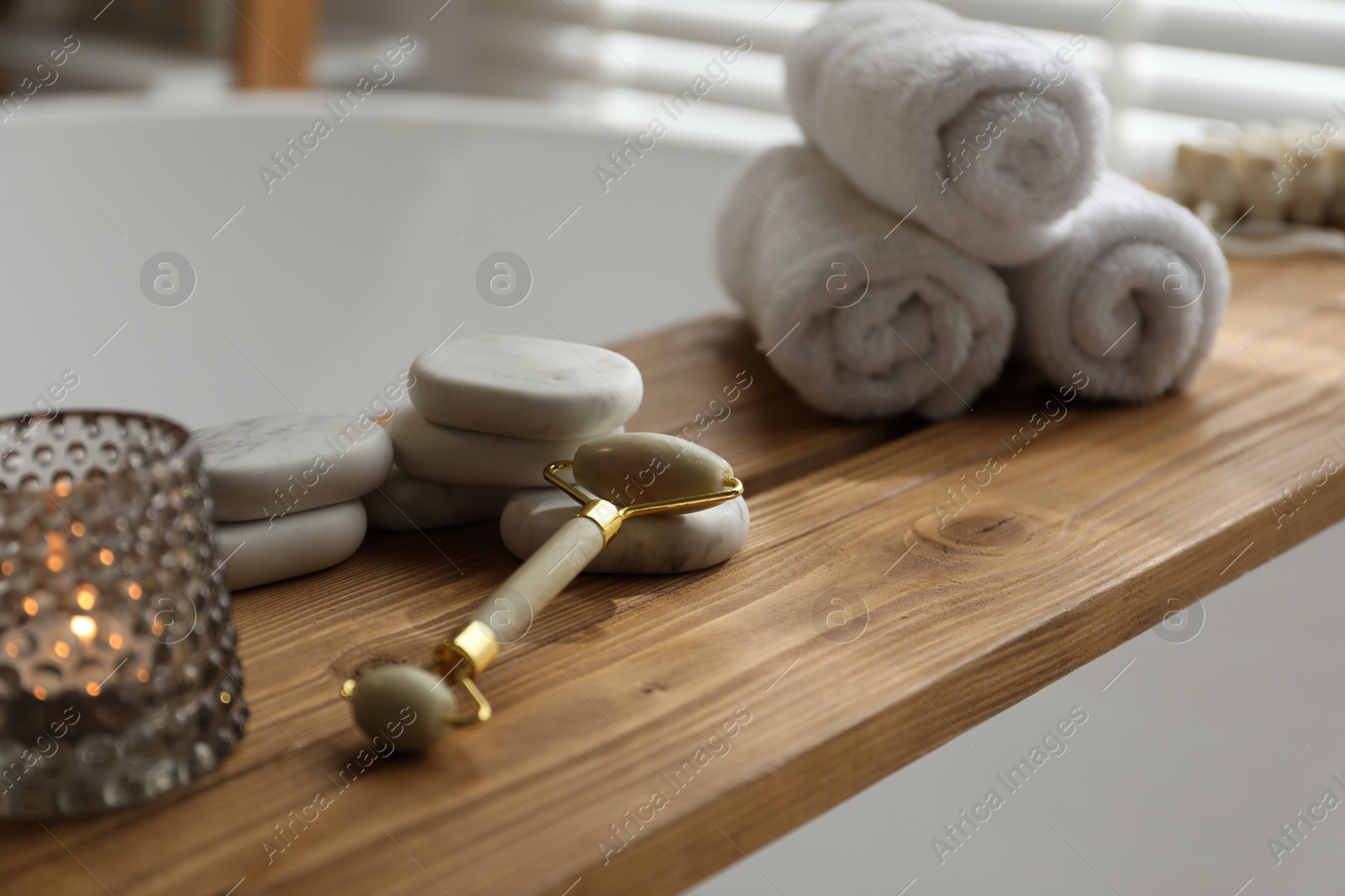Photo of Wooden tray with spa products and burning candle on bath tub, closeup
