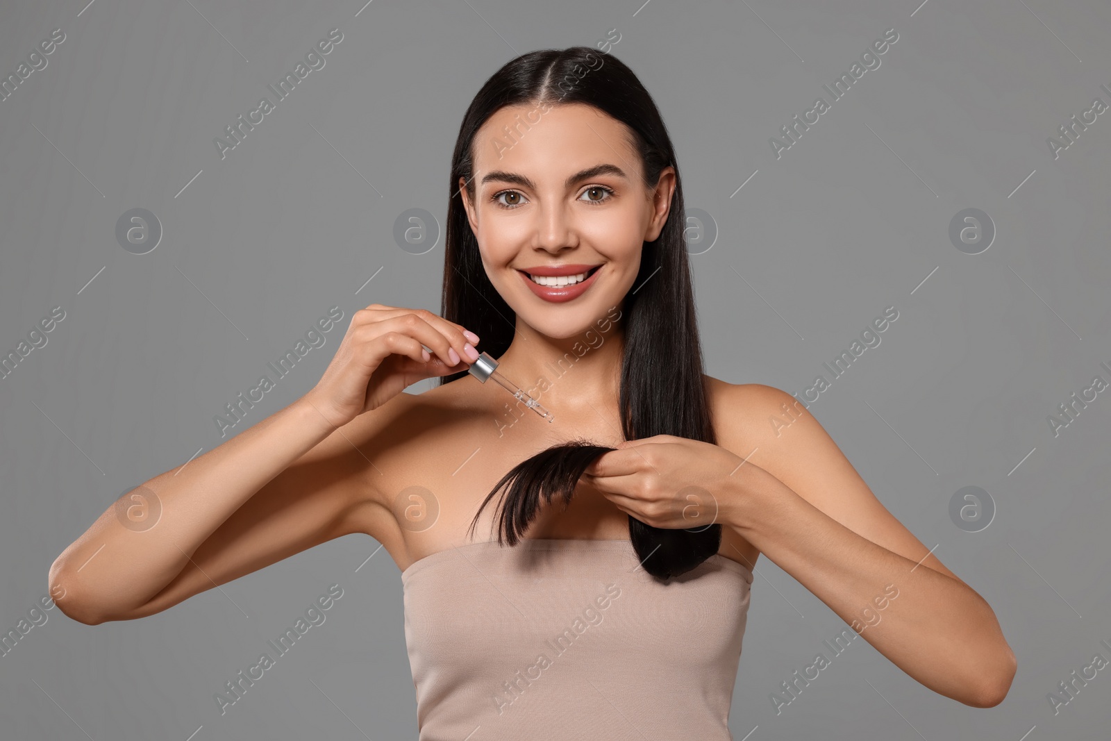 Photo of Beautiful woman applying hair serum on grey background. Cosmetic product