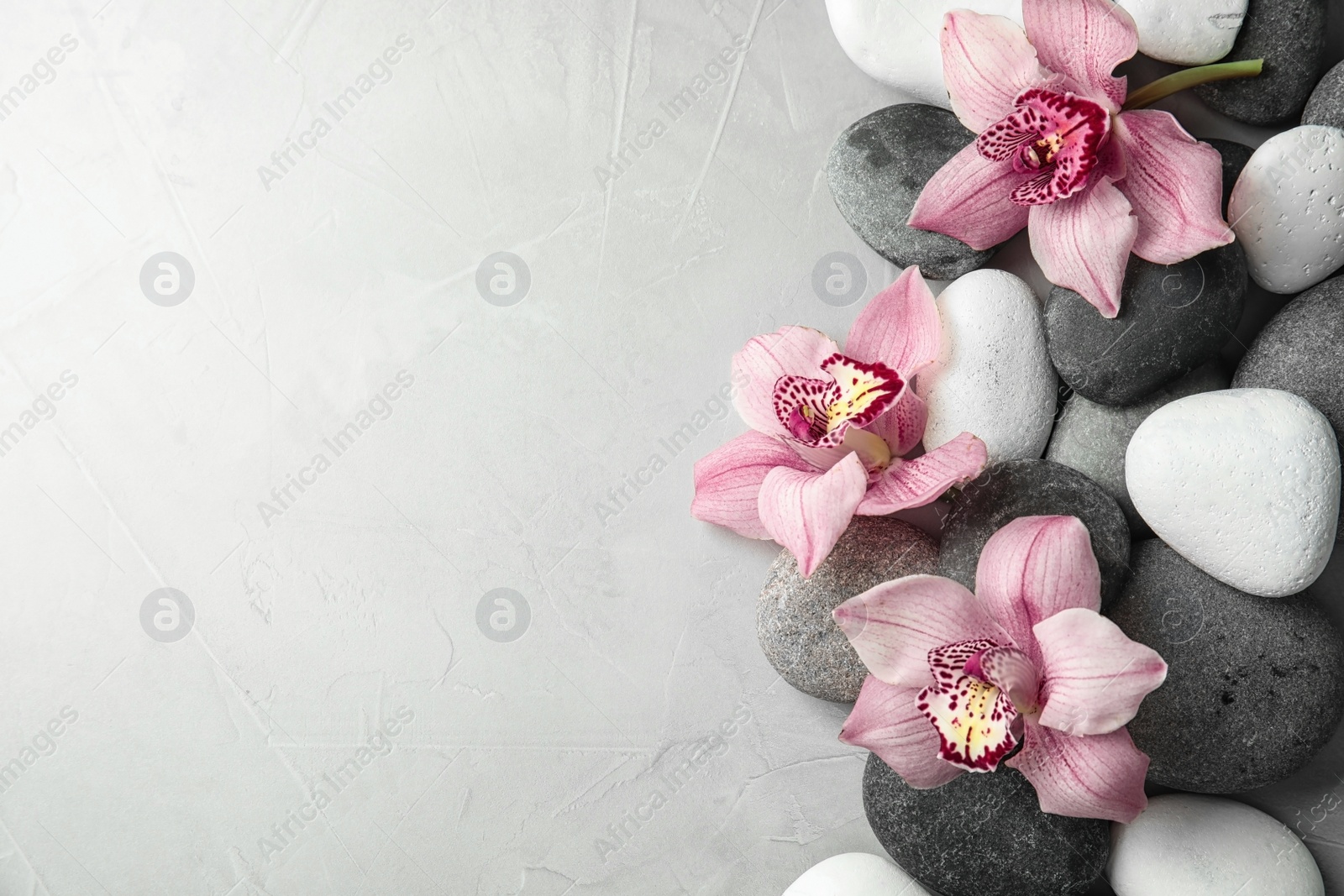 Photo of Zen stones and exotic flowers on grey background, top view with space for text