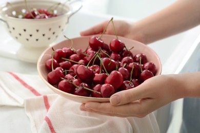 Woman holding bowl with fresh ripe cherries in kitchen, closeup