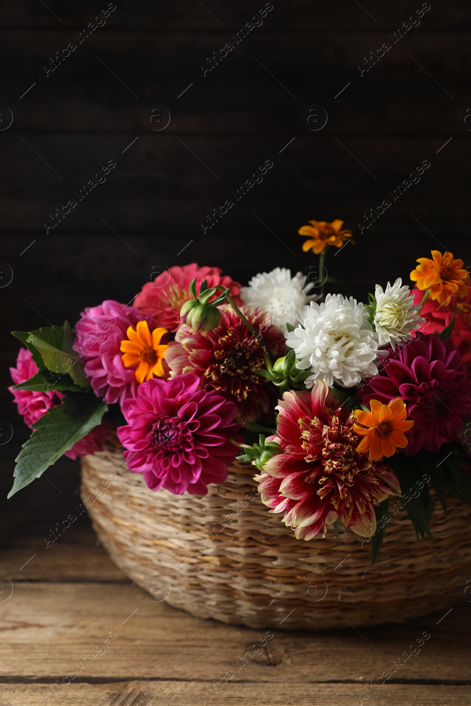 Photo of Beautiful wild flowers and leaves in wicker basket on wooden table, closeup