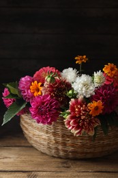 Beautiful wild flowers and leaves in wicker basket on wooden table, closeup