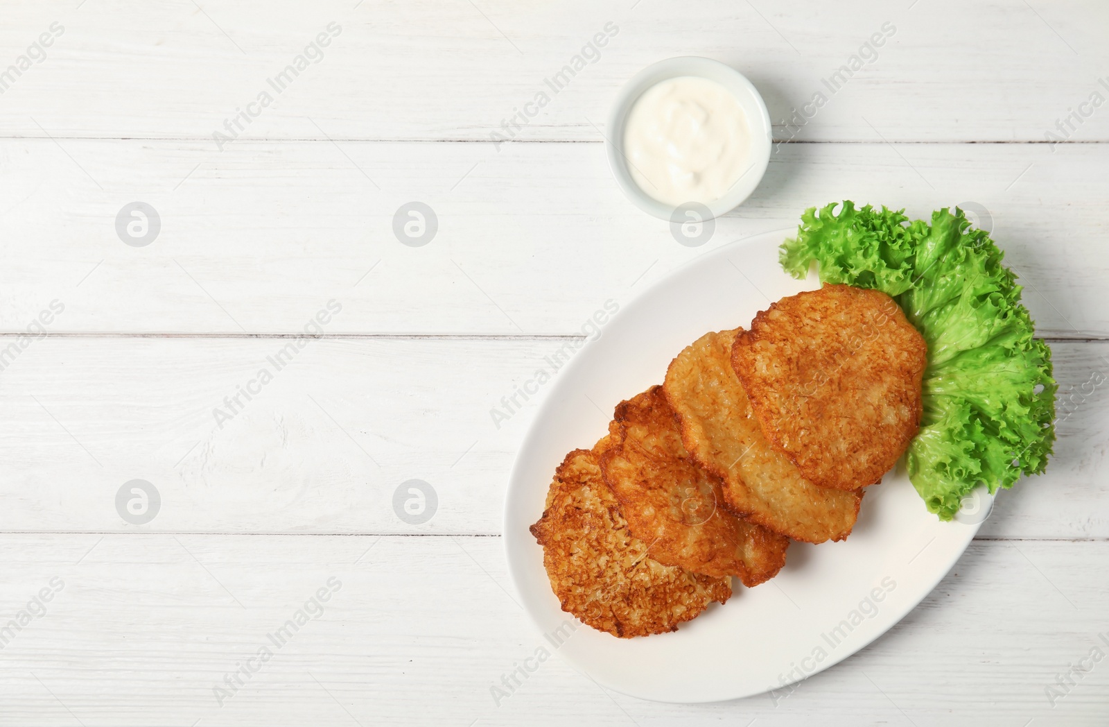 Photo of Plate with tasty potato fritters and sauce on wooden table, top view