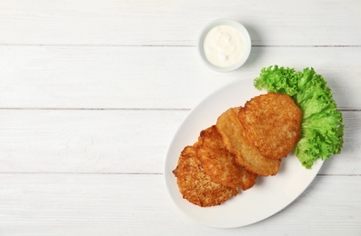 Photo of Plate with tasty potato fritters and sauce on wooden table, top view