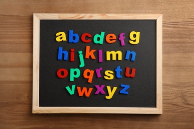 Board with magnetic letters on wooden background, top view. Alphabetical order