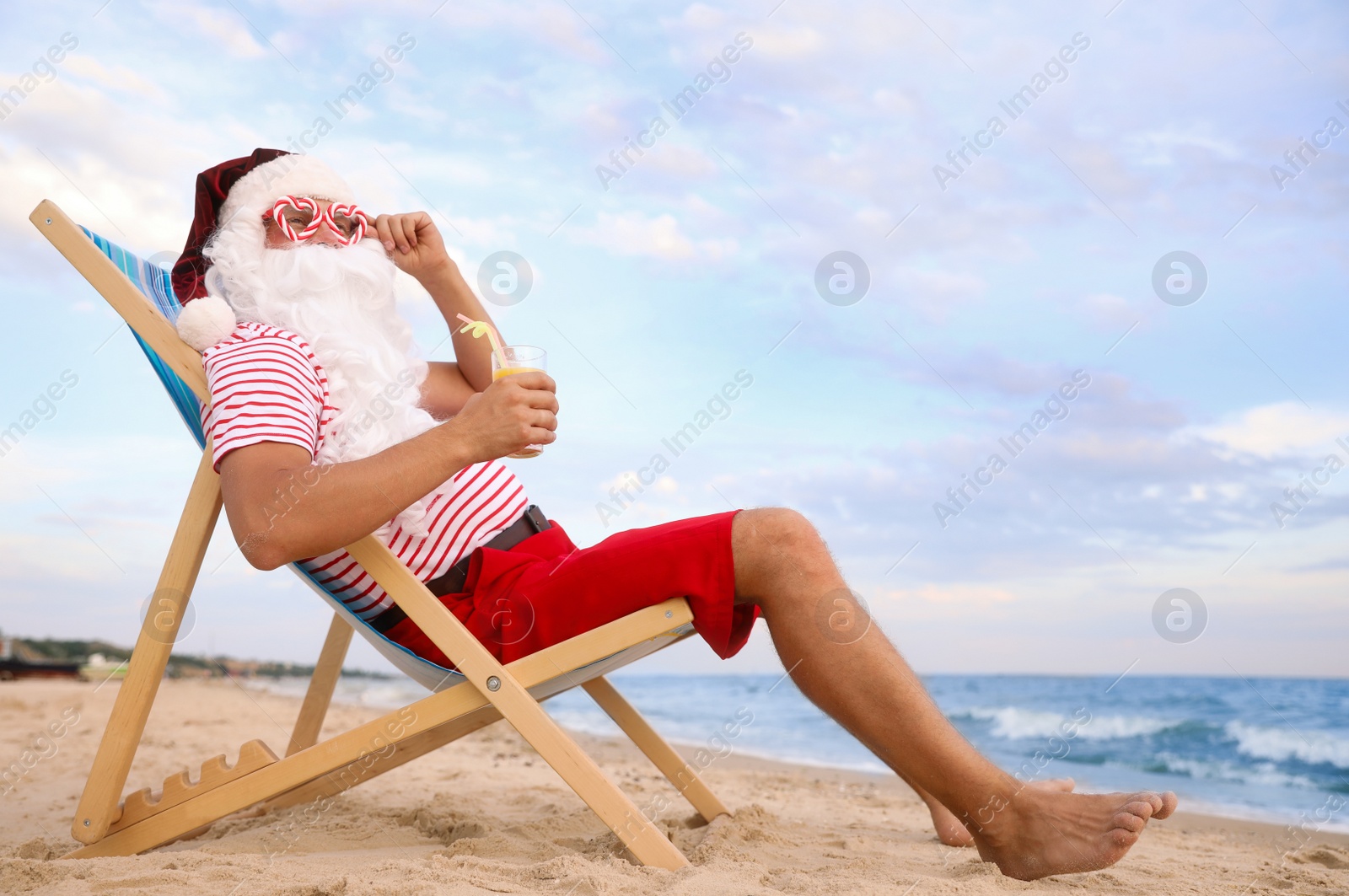 Photo of Santa Claus with cocktail relaxing in chair on beach, space for text. Christmas vacation