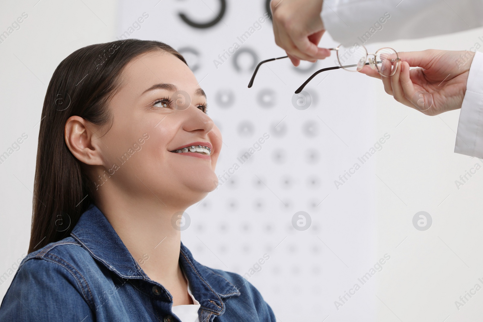 Photo of Vision testing. Ophthalmologist giving glasses to young woman indoors