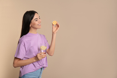 Beautiful young woman with tasty lemon water and fresh fruit on beige background. Space for text