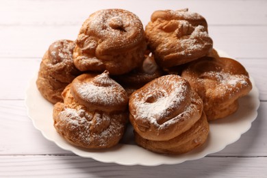 Photo of Delicious profiteroles with powdered sugar on white wooden table