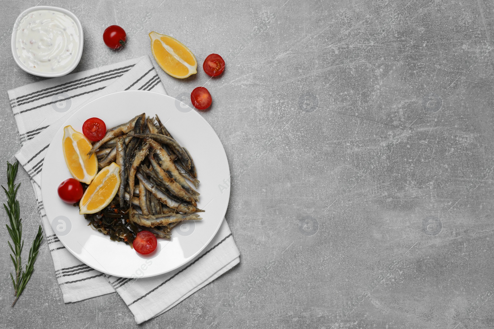 Photo of Delicious fried anchovies with cherry tomatoes and slices of lemon served on light grey table, flat lay. Space for text