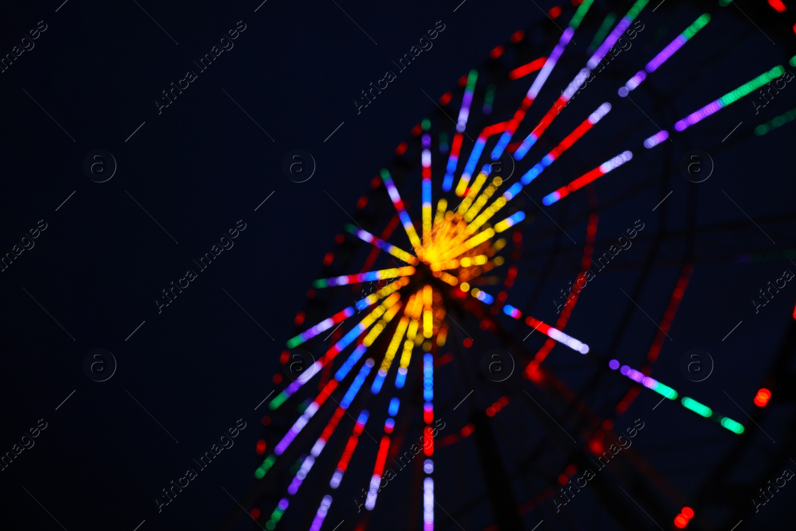 Photo of Blurred view of beautiful glowing Ferris wheel against dark sky. Space for text