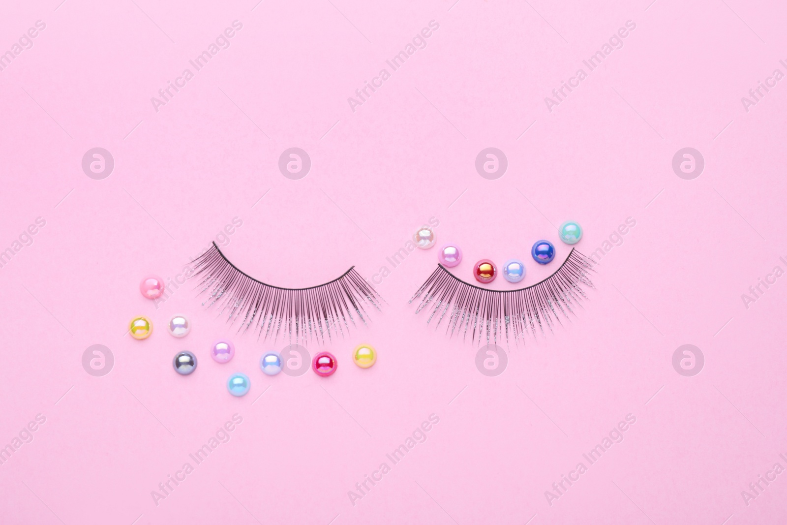 Photo of False eyelashes and colorful beads on pink background, flat lay