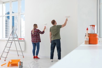 Photo of Couple painting wall in apartment during repair, back view