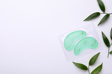 Photo of Package with under eye patches and green twigs on white background, flat lay. Space for text