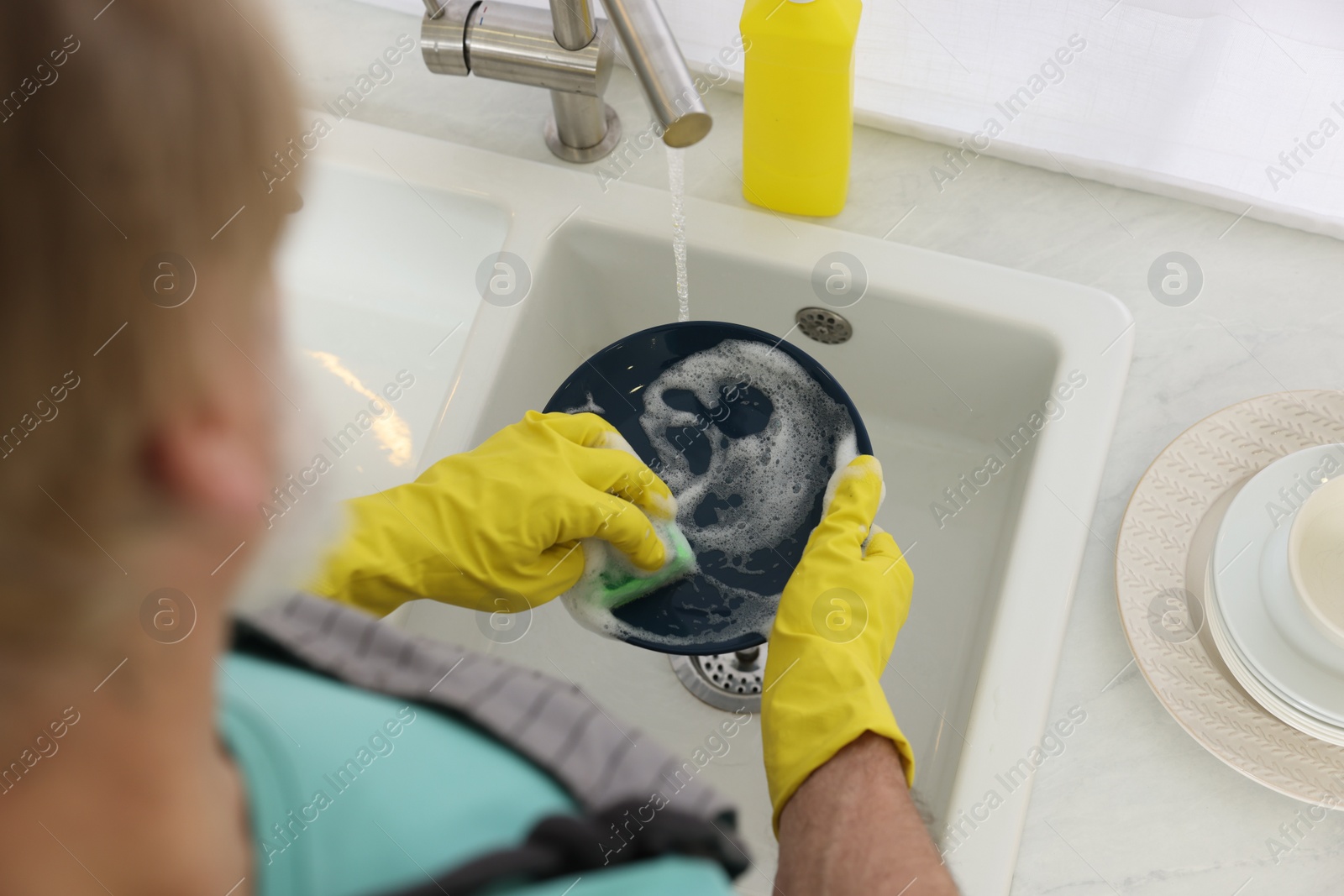 Photo of Man in protective gloves washing plate above sink indoors, closeup