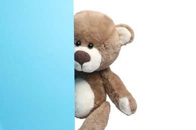 Photo of Cute teddy bear standing behind blank card isolated on white, space for text