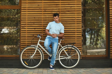 Handsome young hipster man with bicycle near wooden wall outdoors