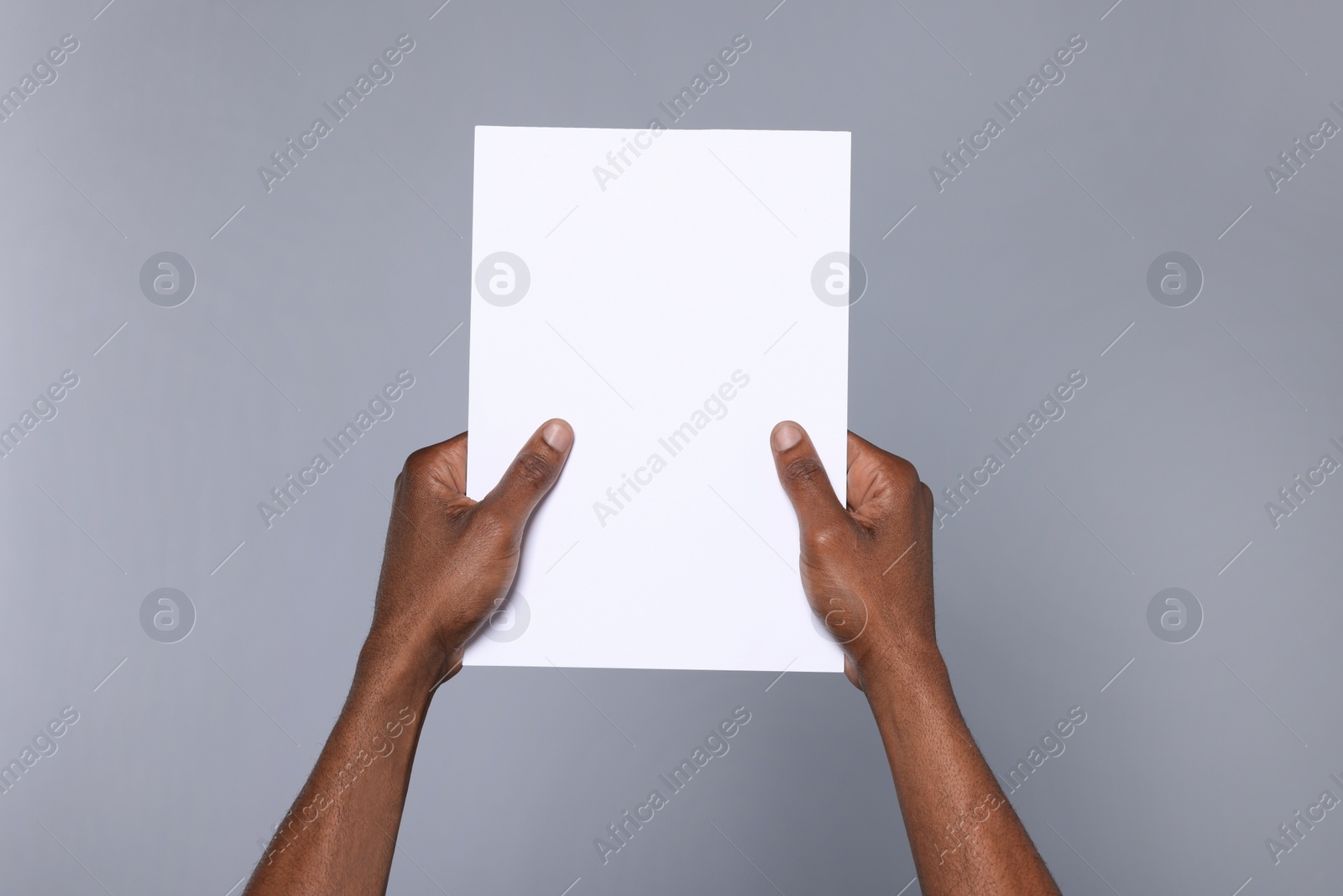 Photo of African American man holding sheet of paper on grey background, closeup. Mockup for design