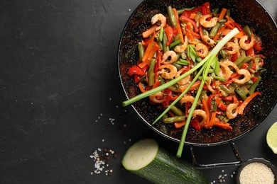 Shrimp stir fry with vegetables in wok and ingredients on black table, flat lay