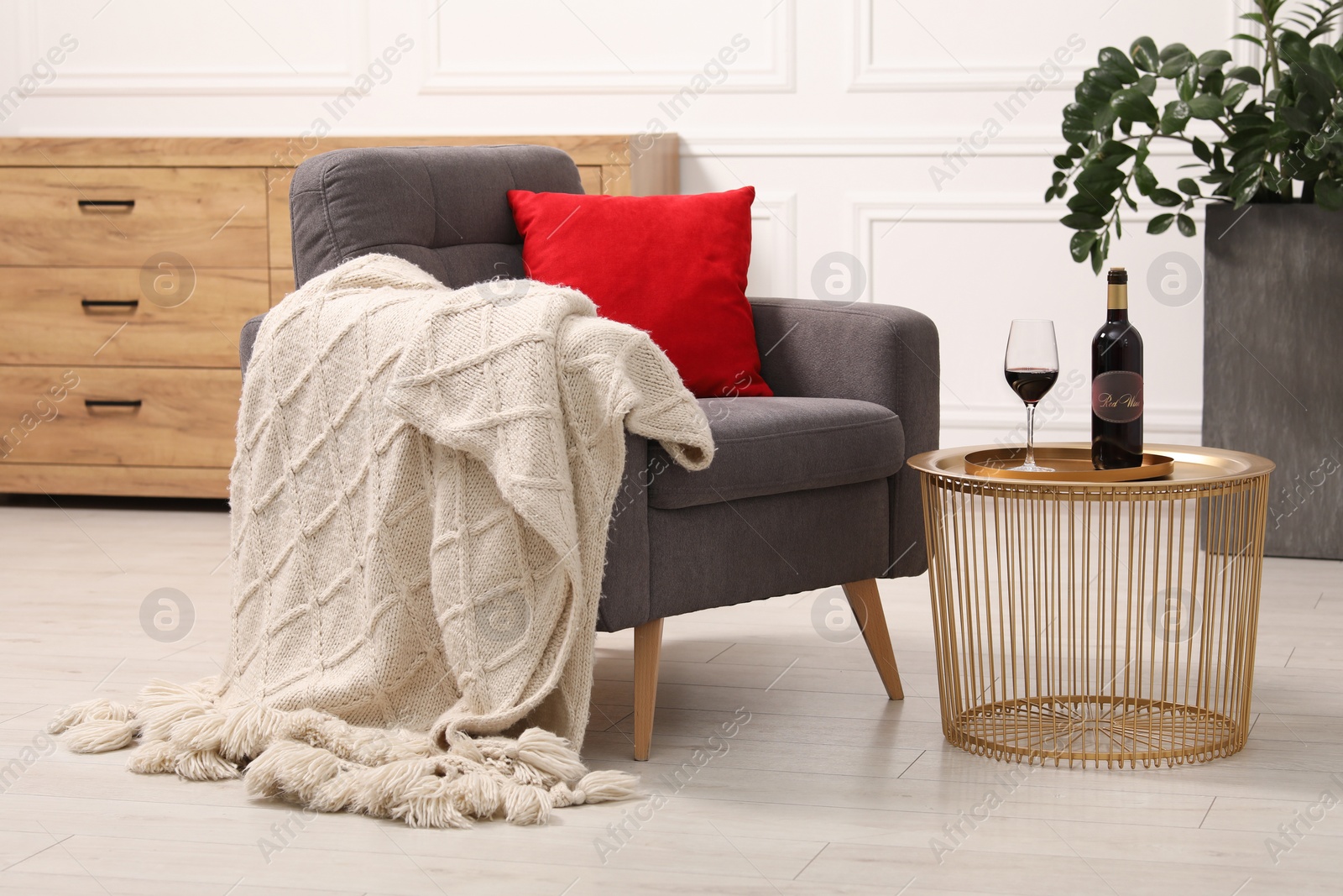 Photo of Stylish living room interior with comfortable armchair, blanket, side table and houseplant