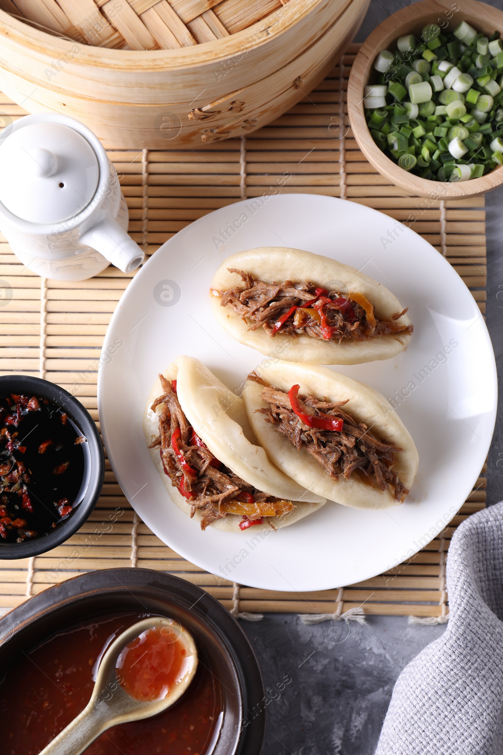 Photo of Delicious gua bao (pork belly buns), green onion and sauce on grey textured table, flat lay
