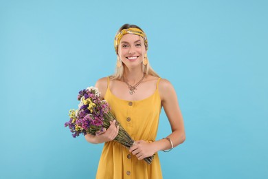 Photo of Portrait of smiling hippie woman with bouquet of flowers on light blue background