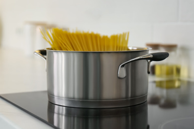 Photo of Saucepan with uncooked pasta on stove in kitchen, closeup