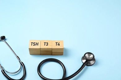 Endocrinology. Stethoscope and wooden cubes with thyroid hormones on light blue background. Space for text