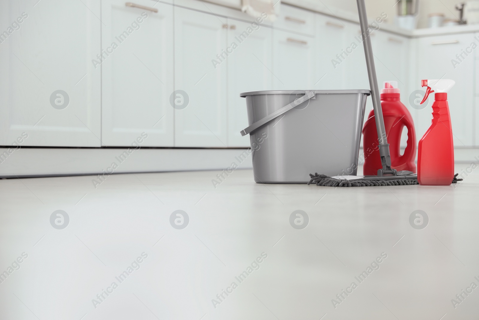 Photo of Mop, detergents and plastic bucket in kitchen, space for text. Cleaning supplies