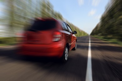 Red car driving at high speed on asphalt road outdoors, motion blur effect
