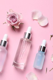 Photo of Bottles of cosmetic serums, flower and petals on pink background, flat lay