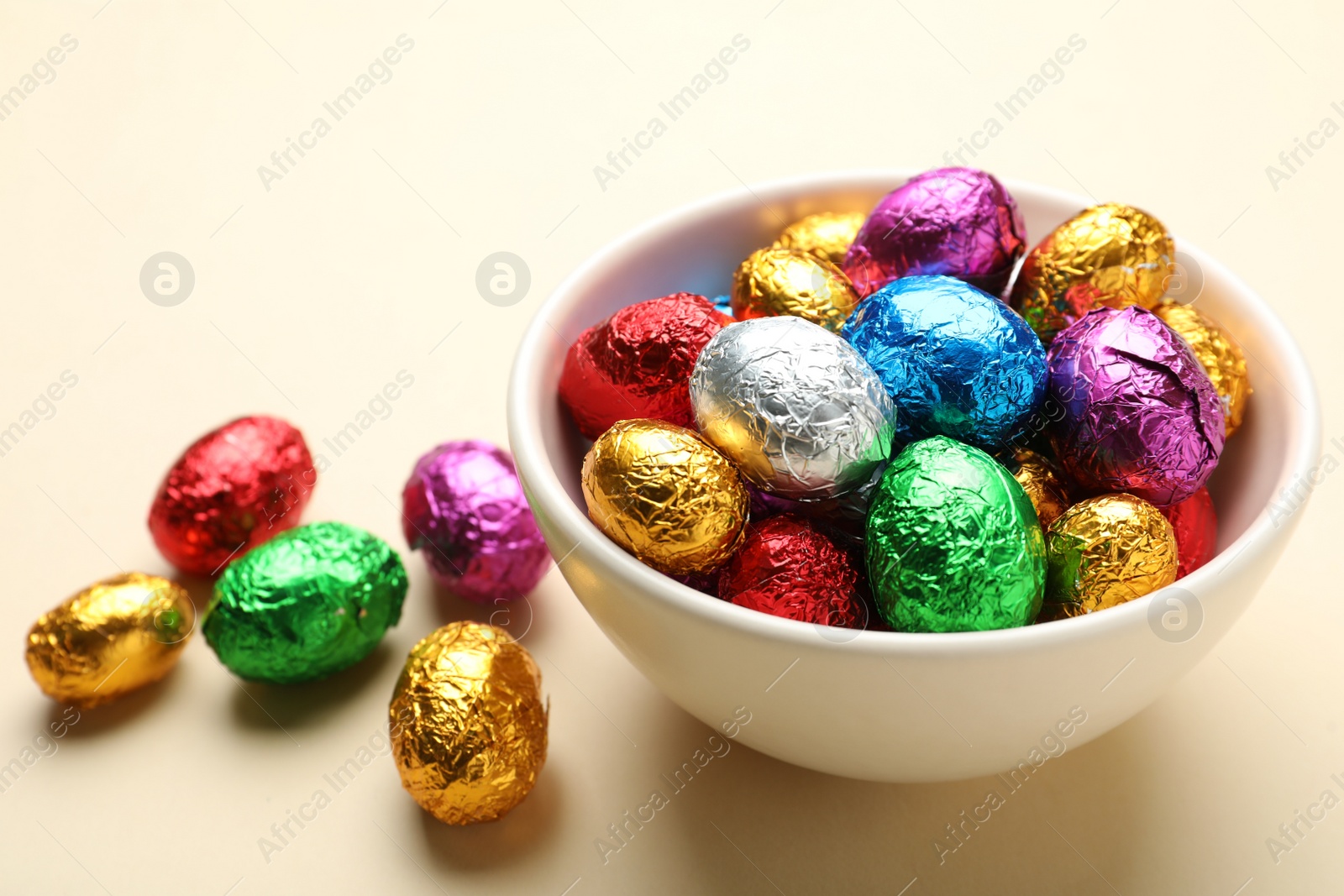 Photo of Chocolate eggs wrapped in colorful foil on beige background