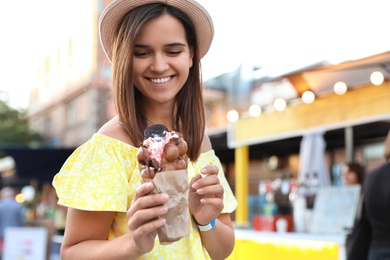 Photo of Pretty young woman holding delicious sweet bubble waffle with ice cream outdoors