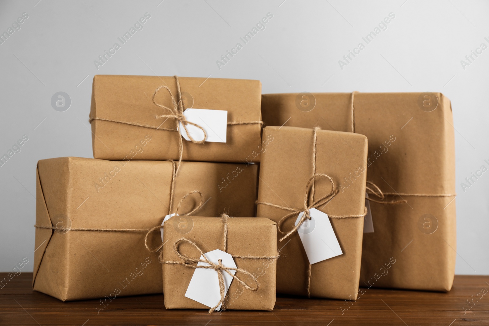 Photo of Parcels wrapped in kraft paper with tags on wooden table against light grey background