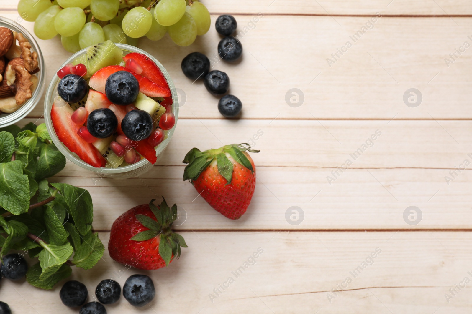 Photo of Delicious fruit salad in glass and ingredients on light wooden table, flat lay. Space for text